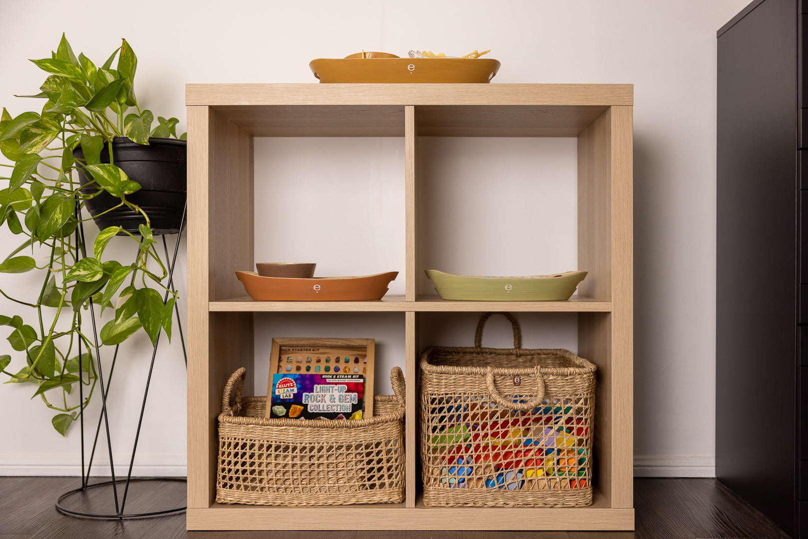 tidy and orderly Montessori play space holding natural baskets and trays on a 4 cube IKEA Kallax shelf