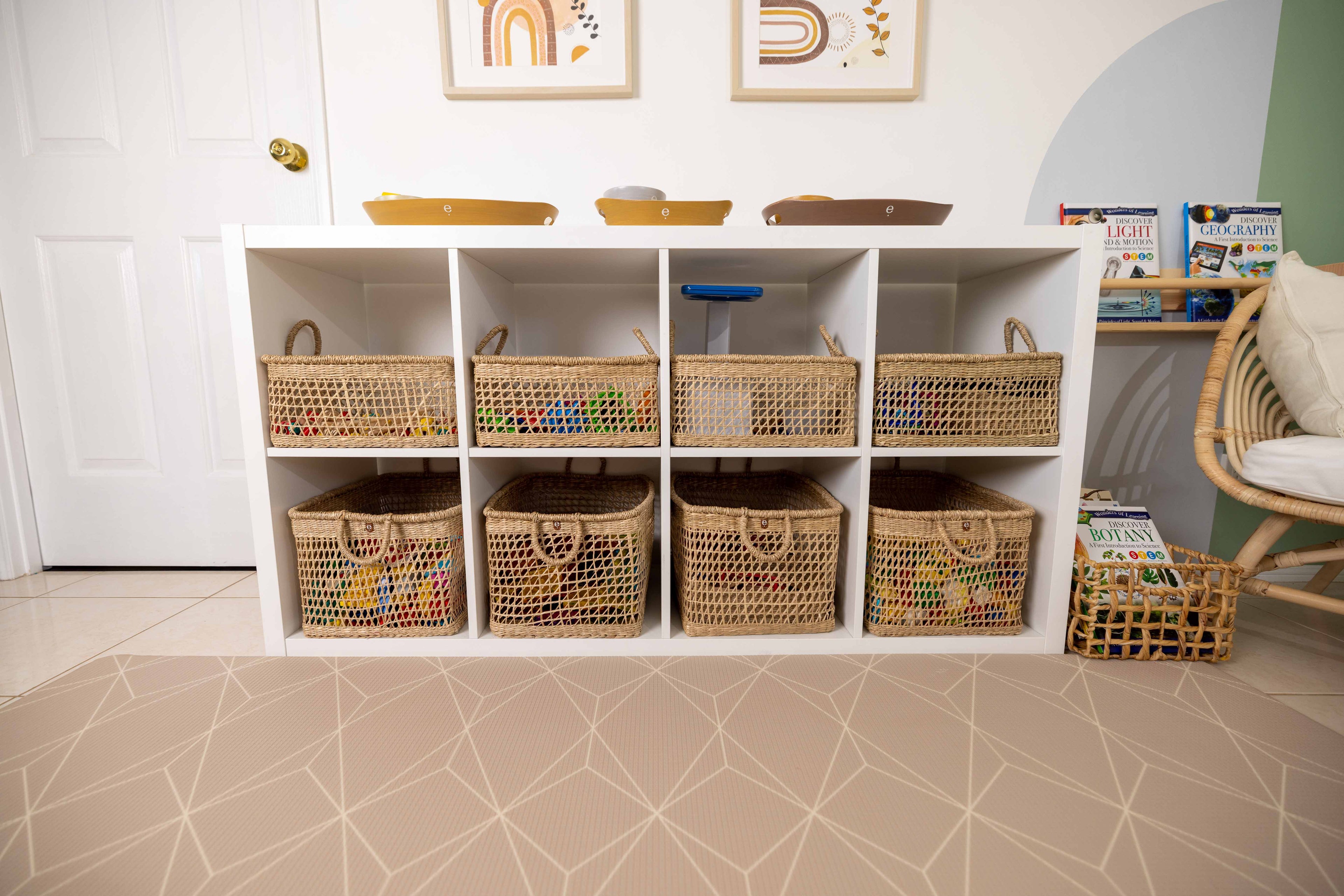 Tidy, orderly and calm play space with activities and toys placed inside matching natural baskets and trays displayed on an IKEA Kallax shelf